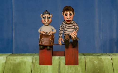 Mousssong Theater mit Figuren, Bild aus "Der Talentdieb": der Schutzdodel, ein graues Männchen mit Aktentasche und nach oben spitz frisierten Haaren und der Junge Jim sitzen auf dem Dach